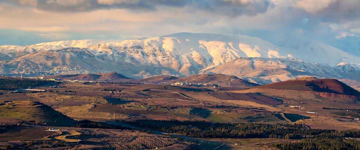 A snow-capped mountain range with terraced fields and a cloudy sky.