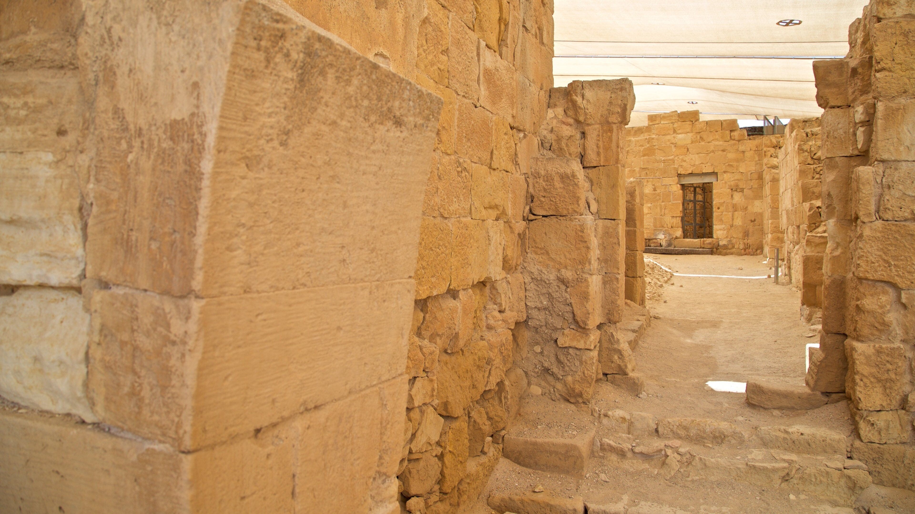 An ancient stone corridor with large, uneven walls and a sandy floor.