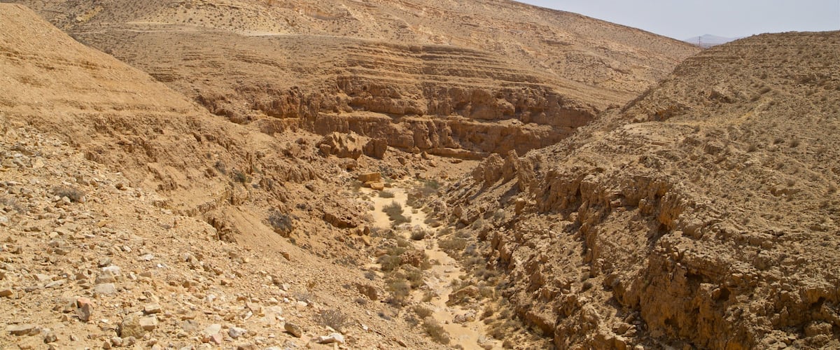 A rugged desert landscape with rocky terrain and a prominent hill in the background.