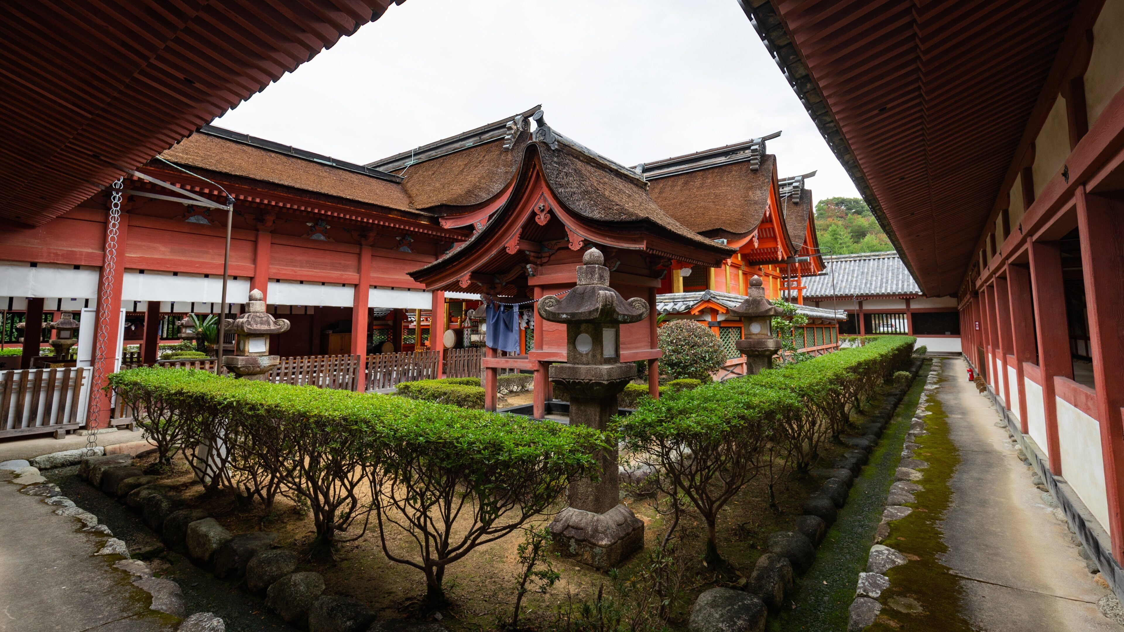 Een traditionele Japanse tempel met rode houten constructies, een stenen lantaarn en een verzorgde tuin met rotsen en bomen.