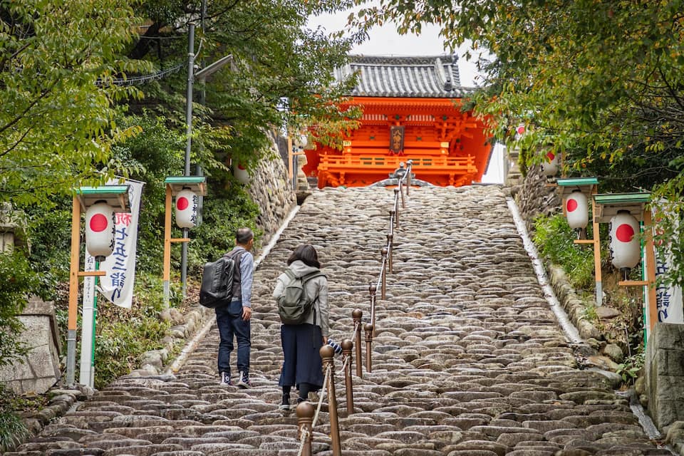 Un escalier en pierre menant à une porte traditionnelle japonaise surmontée d’un torii rouge.