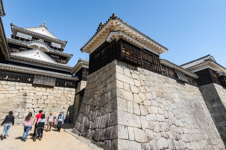 Un castillo japonés tradicional con muros de piedra y varios tejados con tejas.