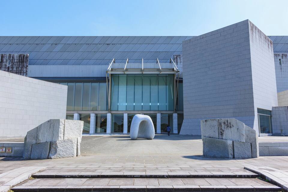 A modern building with large glass windows and a unique sculpture in front.