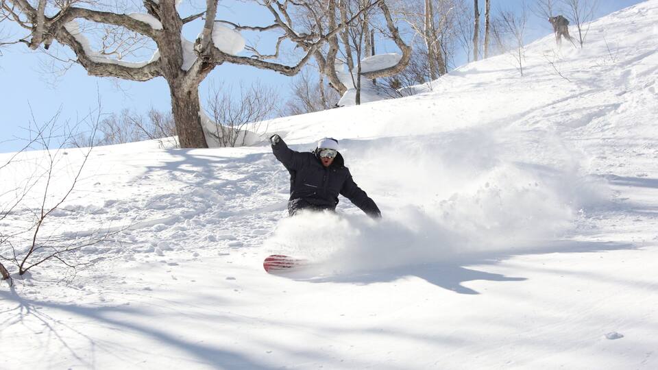 A person snowboarding down a snowy slope with trees in the background.