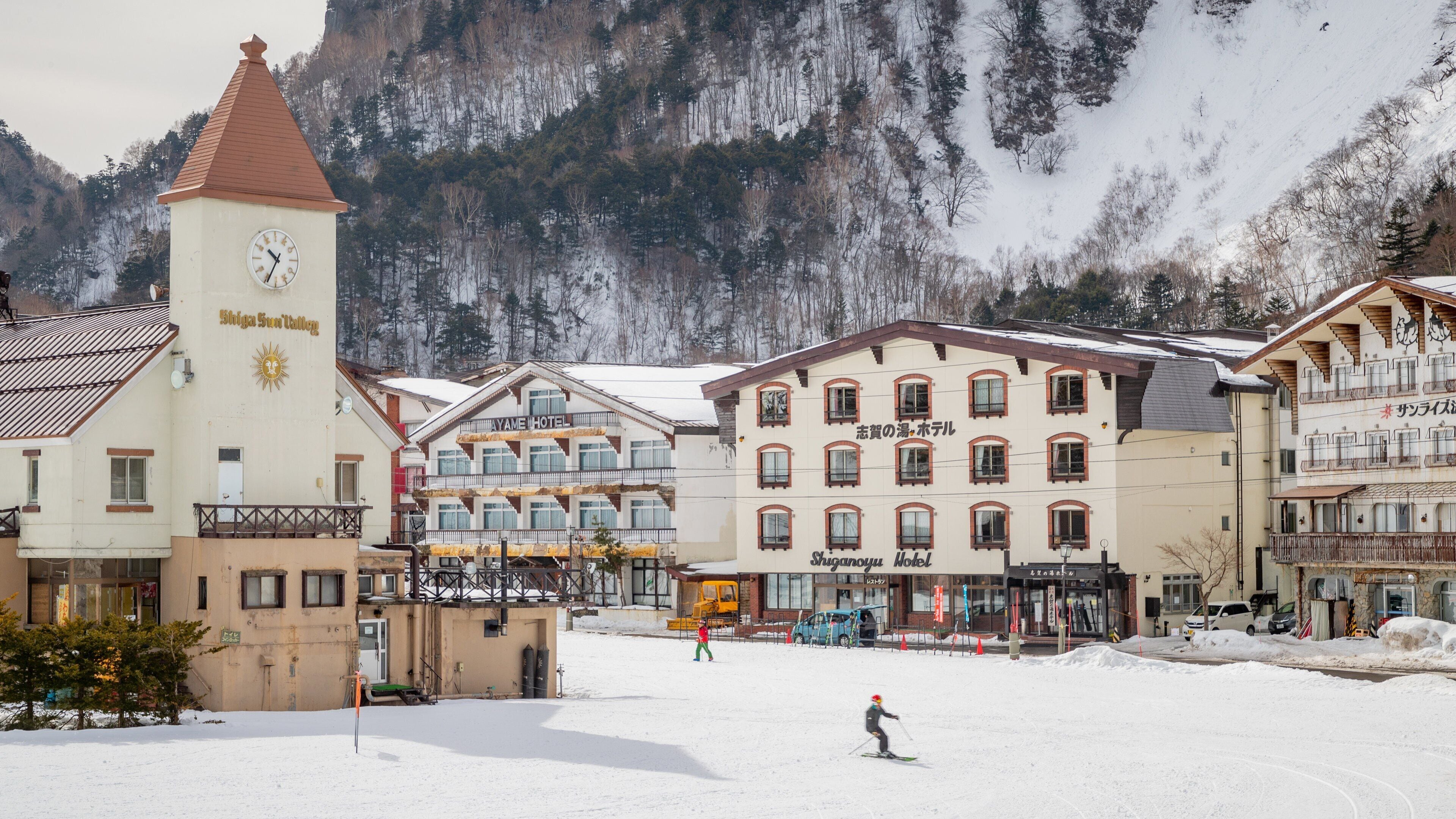 A snowy town with a clock tower, a ski resort, and a mountain backdrop.