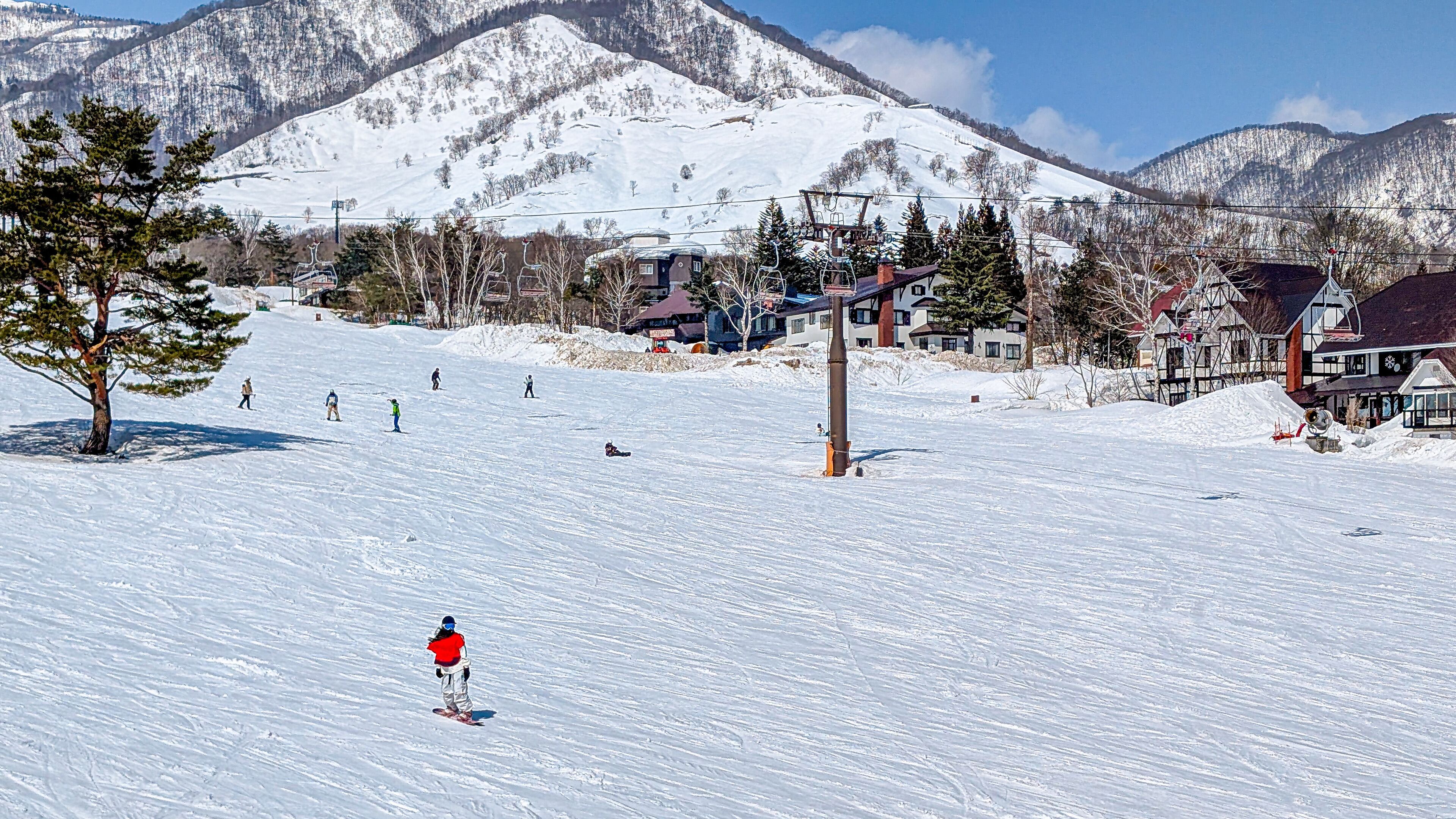 Skiers on ski slope with jagged mountain backdrop. Hakuba, Japan