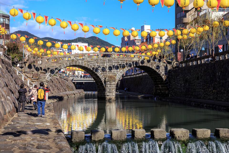 A stone bridge over a river with yellow lanterns and red banners.