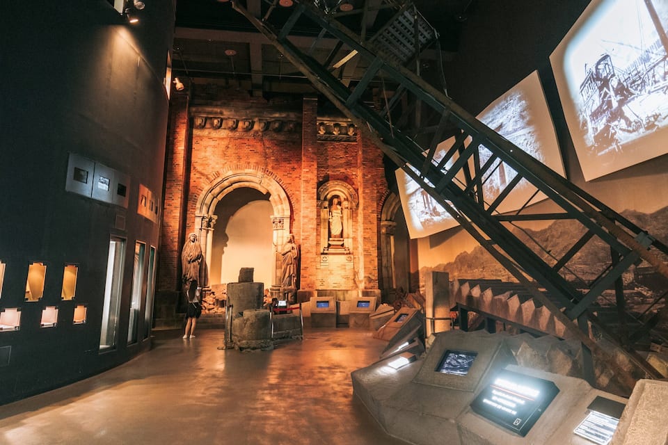 Un museo interno con pareti in mattoni, una scala e statue in pietra.
