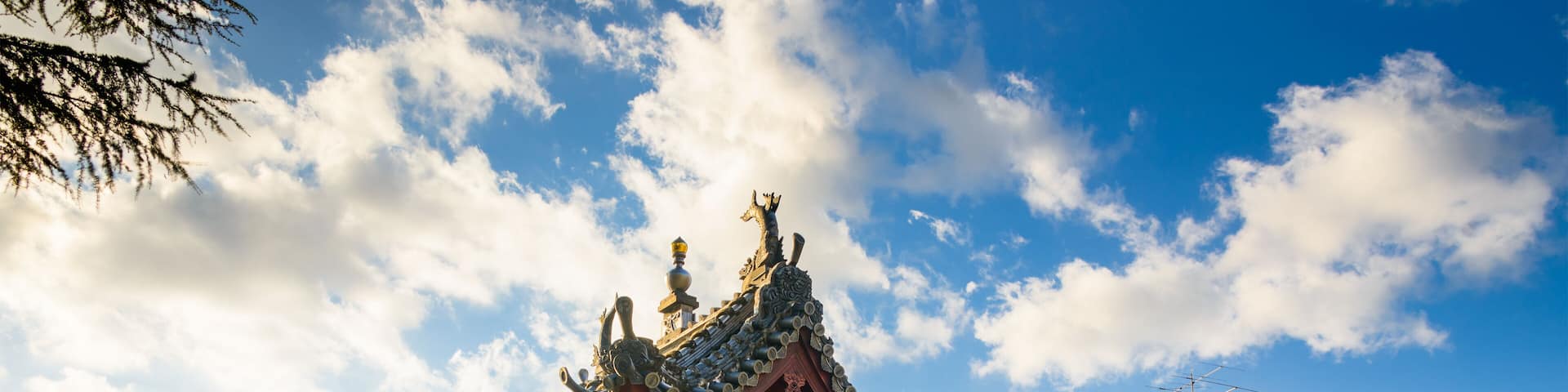 A traditional Chinese pagoda with ornate roof tiles and a red base, surrounded by modern buildings.