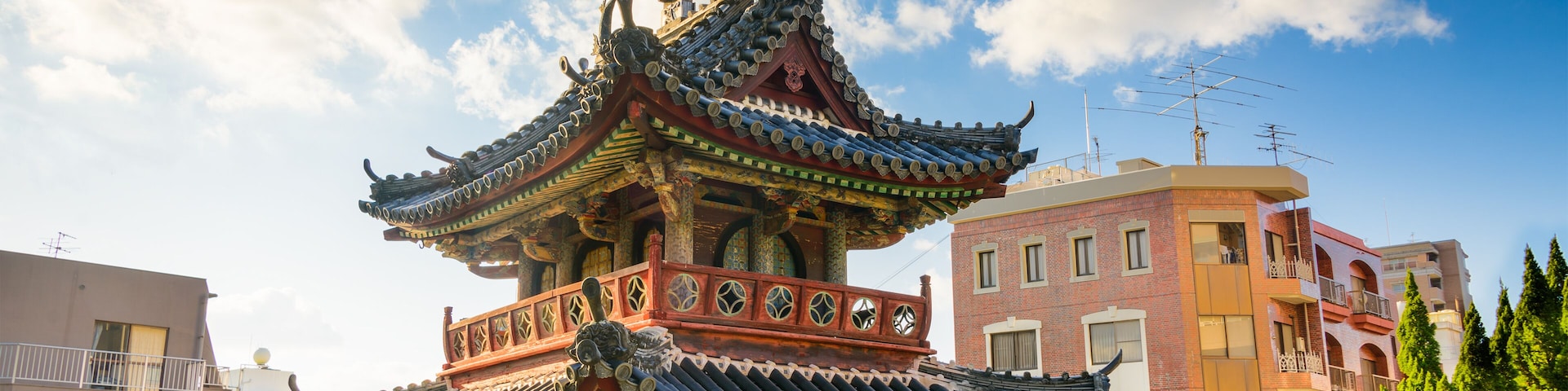 Uma pagoda chinesa tradicional com telhas ornamentais e base vermelha, rodeada por edifícios modernos.