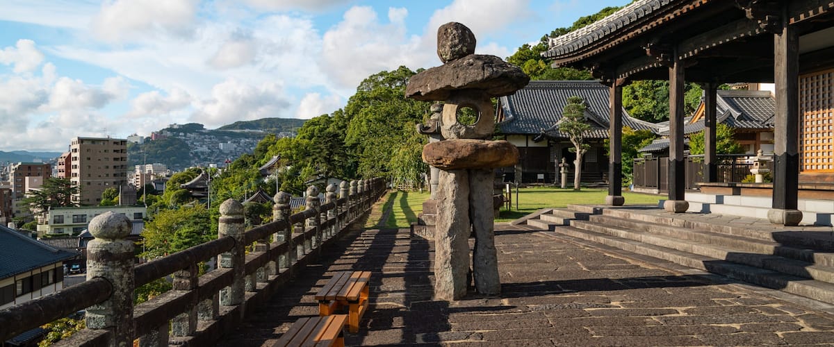 A traditional Japanese stone lantern, a wooden fence, and a temple with tiled roofs.