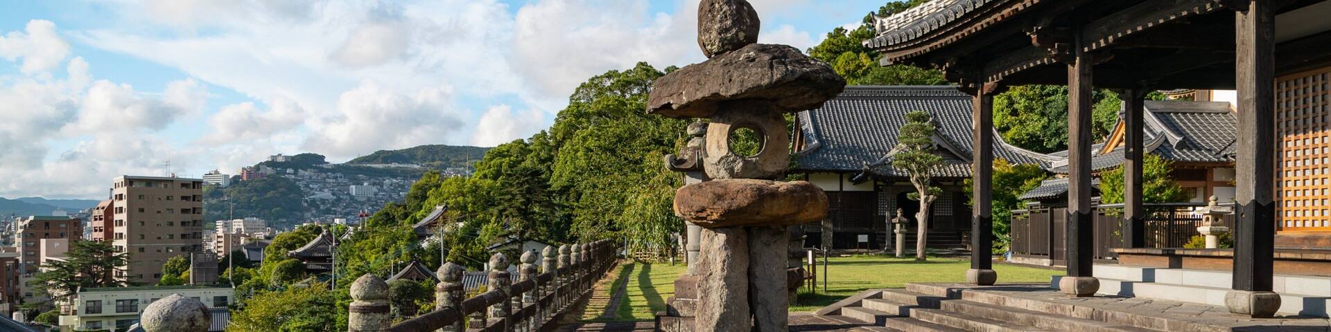 A traditional Japanese stone lantern, a wooden fence, and a temple with tiled roofs.