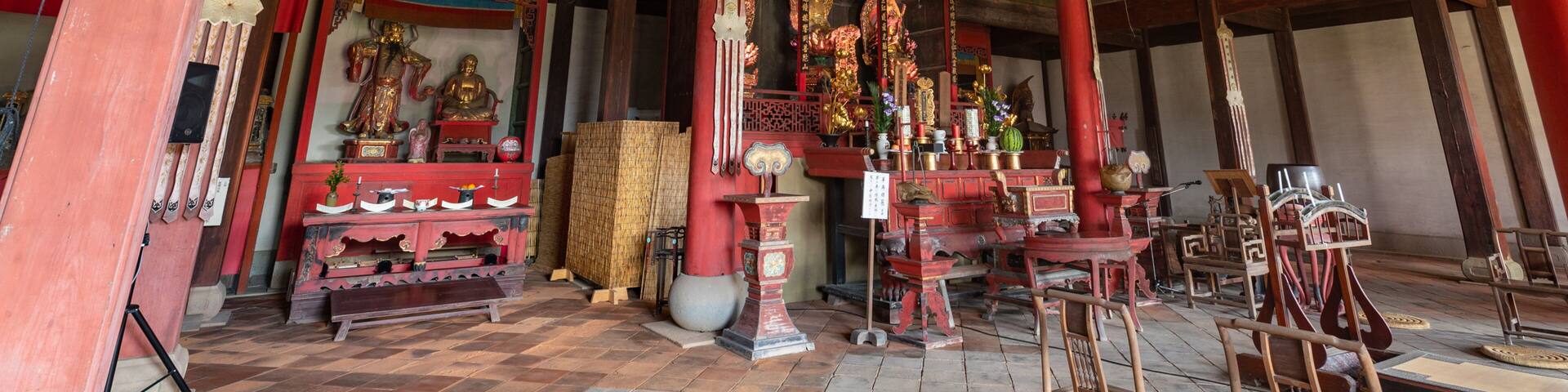 A traditional wooden temple interior with statues, incense burners, and ritual objects.