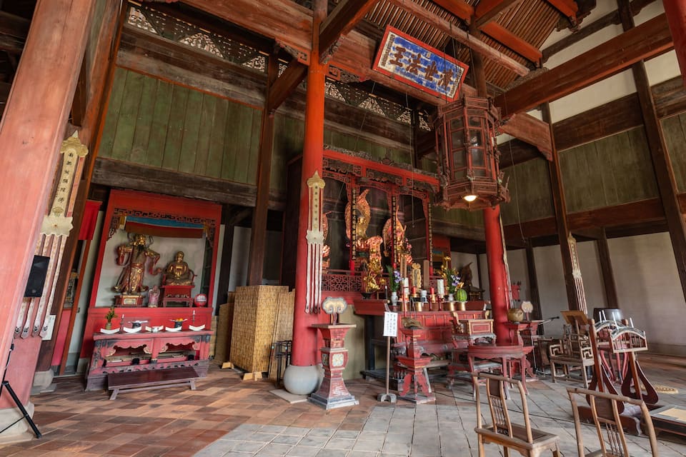 A traditional wooden temple interior with statues, incense burners, and ritual objects.