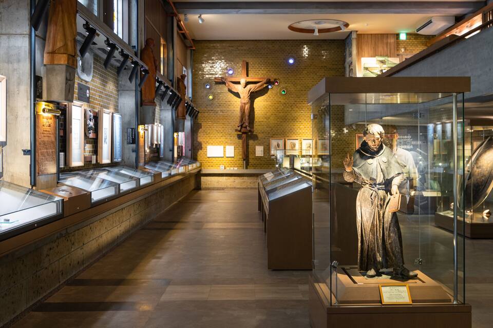 Interior de museo con un crucifijo, vitrinas de cristal y paneles informativos.