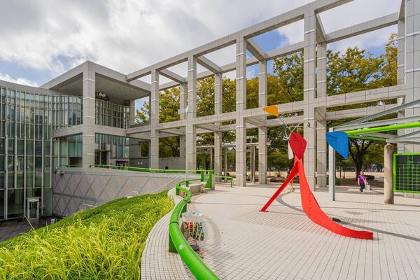 Un moderno complejo arquitectónico con fachadas de vidrio, un sendero arbolado y esculturas abstractas.
