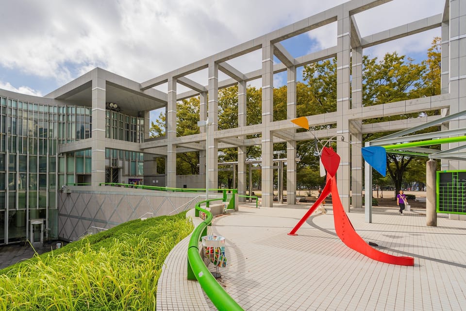 A modern architectural complex with glass facades, a green pathway, and abstract sculptures.