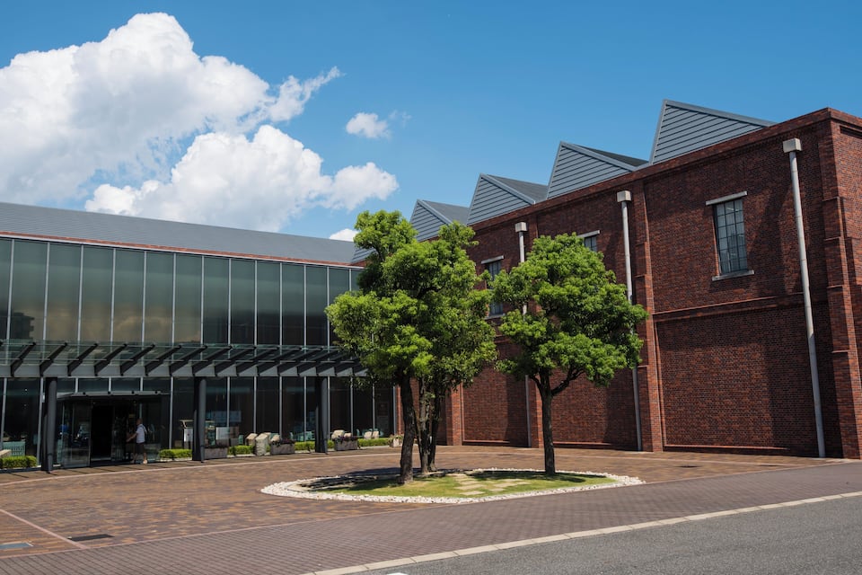 A modern building with glass facade and brick exterior, surrounded by a landscaped area with trees.