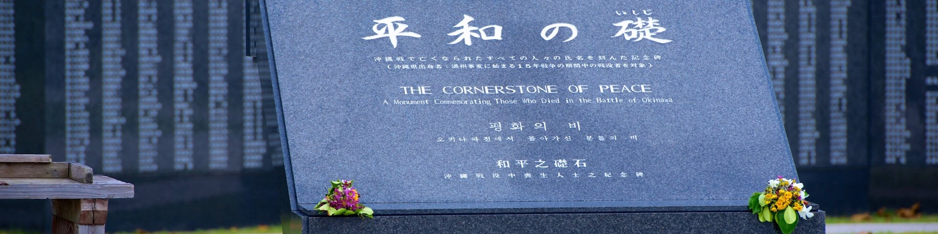 Monumento de piedra con inscripciones en japonés e inglés, rodeado de un área verde con un banco de madera.