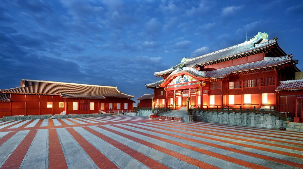 Un temple japonès tradicional amb teulada vermella i decoracions ornamentals, un pati empedrat i un cel blau clar.