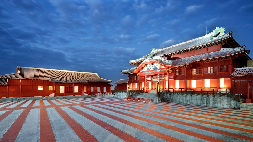 A traditional Japanese temple with a red roof and ornate decorations, a stone-paved courtyard, and a clear blue sky.