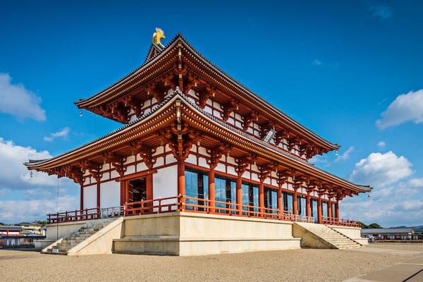 Ein traditionelles japanisches Gebäude mit einem mehrstufigen Dach, roten Säulen und einer Statue auf der Spitze.