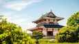 Une pagode japonaise traditionnelle, dotée d’un toit à plusieurs niveaux, entourée d’une végétation luxuriante et surplombée d’un ciel dégagé.