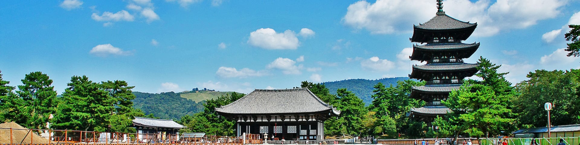 Un templo japonés tradicional con una pagoda de varios niveles, rodeado de un paisaje sereno con árboles y un cielo azul despejado.