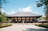 Un bâtiment japonais traditionnel, doté d’un toit en tuiles et de piliers en bois, entouré d’une cour de gravier et d’arbres.