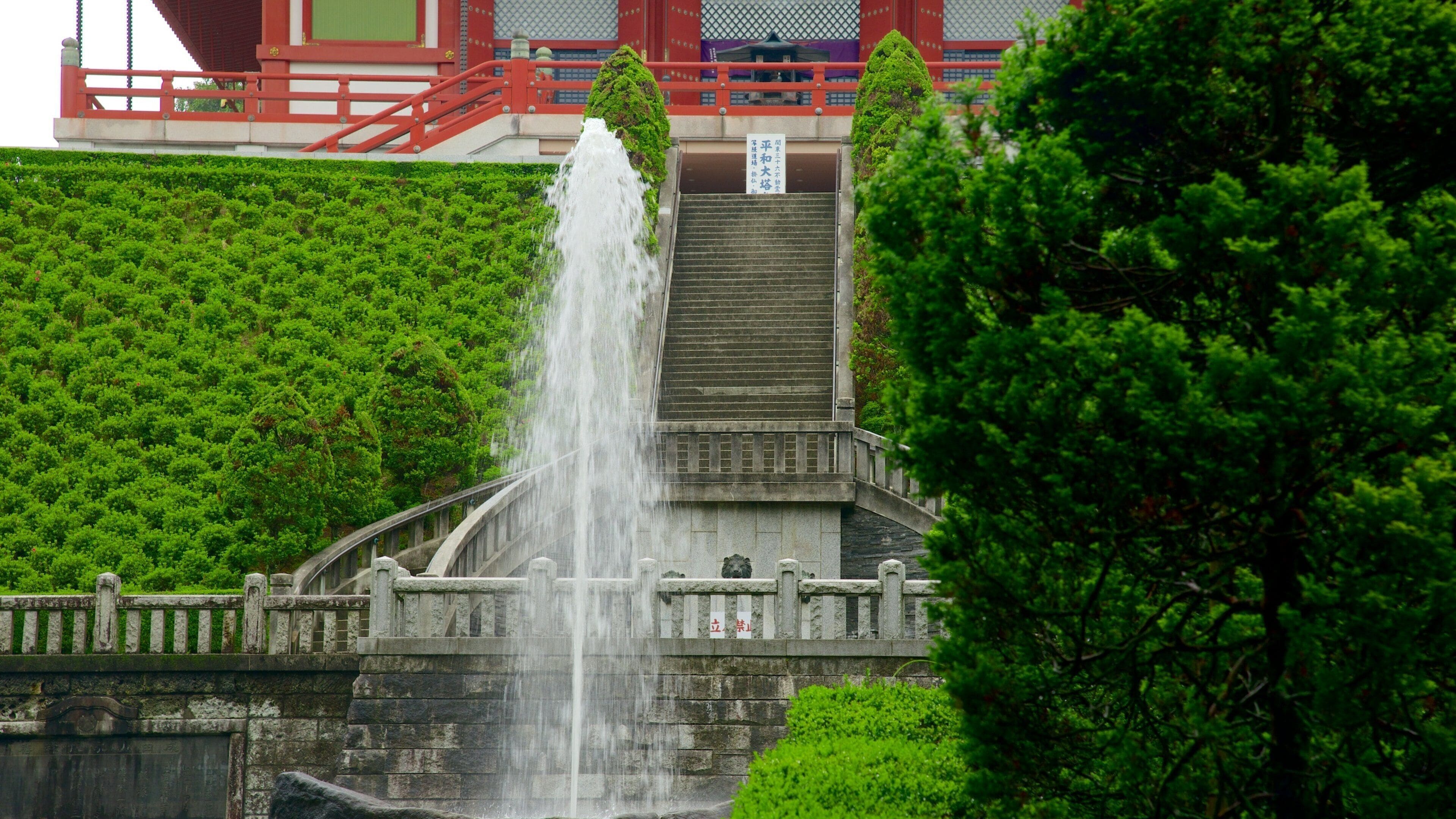 A traditional Japanese stone bridge with a waterfall, surrounded by lush greenery.