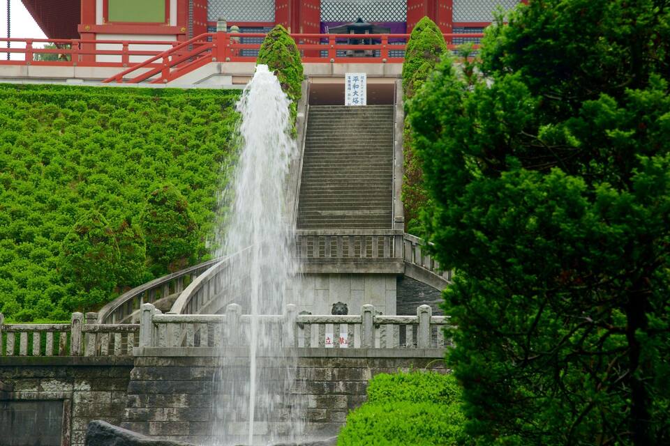 Un puente de piedra japonés tradicional con una cascada, rodeado de abundante vegetación.