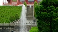 A traditional Japanese stone bridge with a waterfall, surrounded by lush greenery.