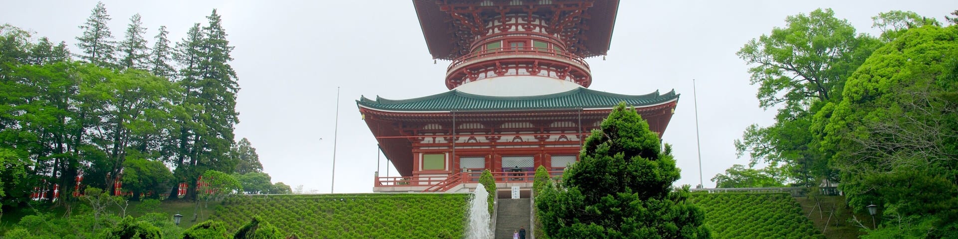 A traditional Japanese pagoda with a golden spire, surrounded by lush greenery and a stone staircase leading up to it.