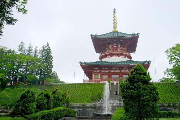 Eine traditionelle japanische Pagode mit goldener Spitze, umgeben von üppigem Grün und einer Steintreppe, die dorthin führt.
