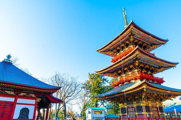 Um pagode tradicional de vários níveis, com detalhes intrincados em vermelho e dourado, rodeado por árvores e um céu azul límpido.