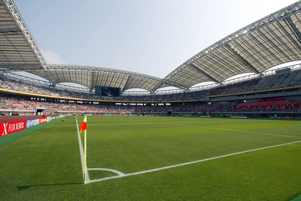 A large stadium with a green field, a red flag, and advertisements on the stands.