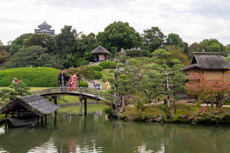 A traditional Japanese garden with a stone bridge, koi fish pond, and various trees and shrubs.