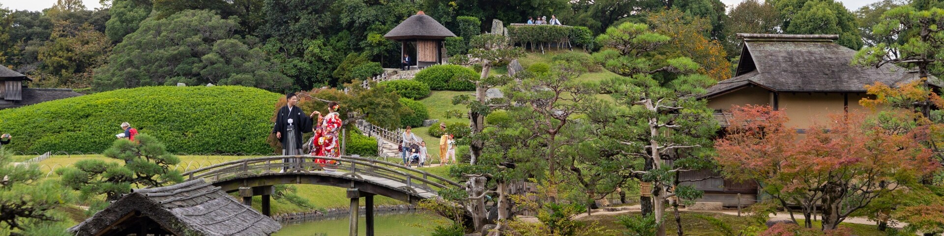 Um jardim japonês tradicional com uma ponte de pedra, lago de carpas koi e diversas árvores e arbustos.