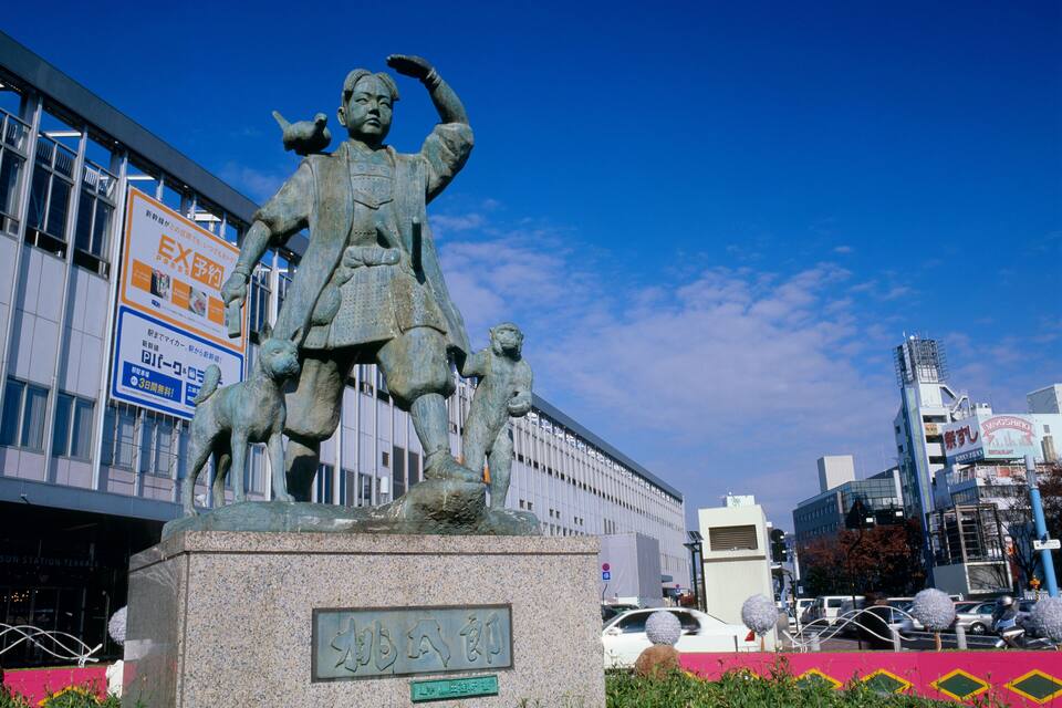 A statue of a historical figure with children, set against a modern cityscape with buildings and a clear blue sky.