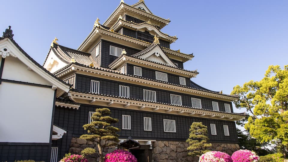 A traditional Japanese castle with multiple tiers, white and black wooden walls, and golden accents.