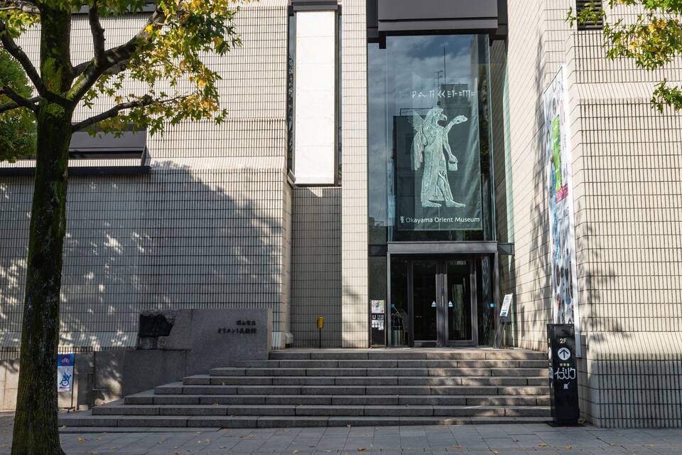Ein Gebäude mit einer großen Glasfassade, Stufen zum Eingang und ein Baum im Vordergrund.