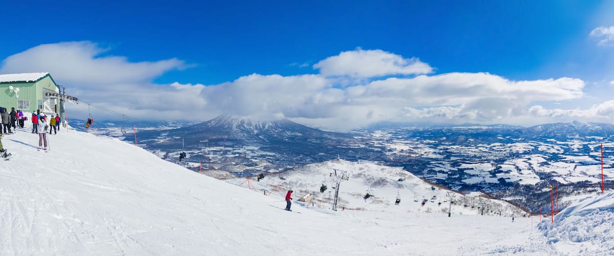 A snow-covered ski slope with a mountain in the background and a clear blue sky.