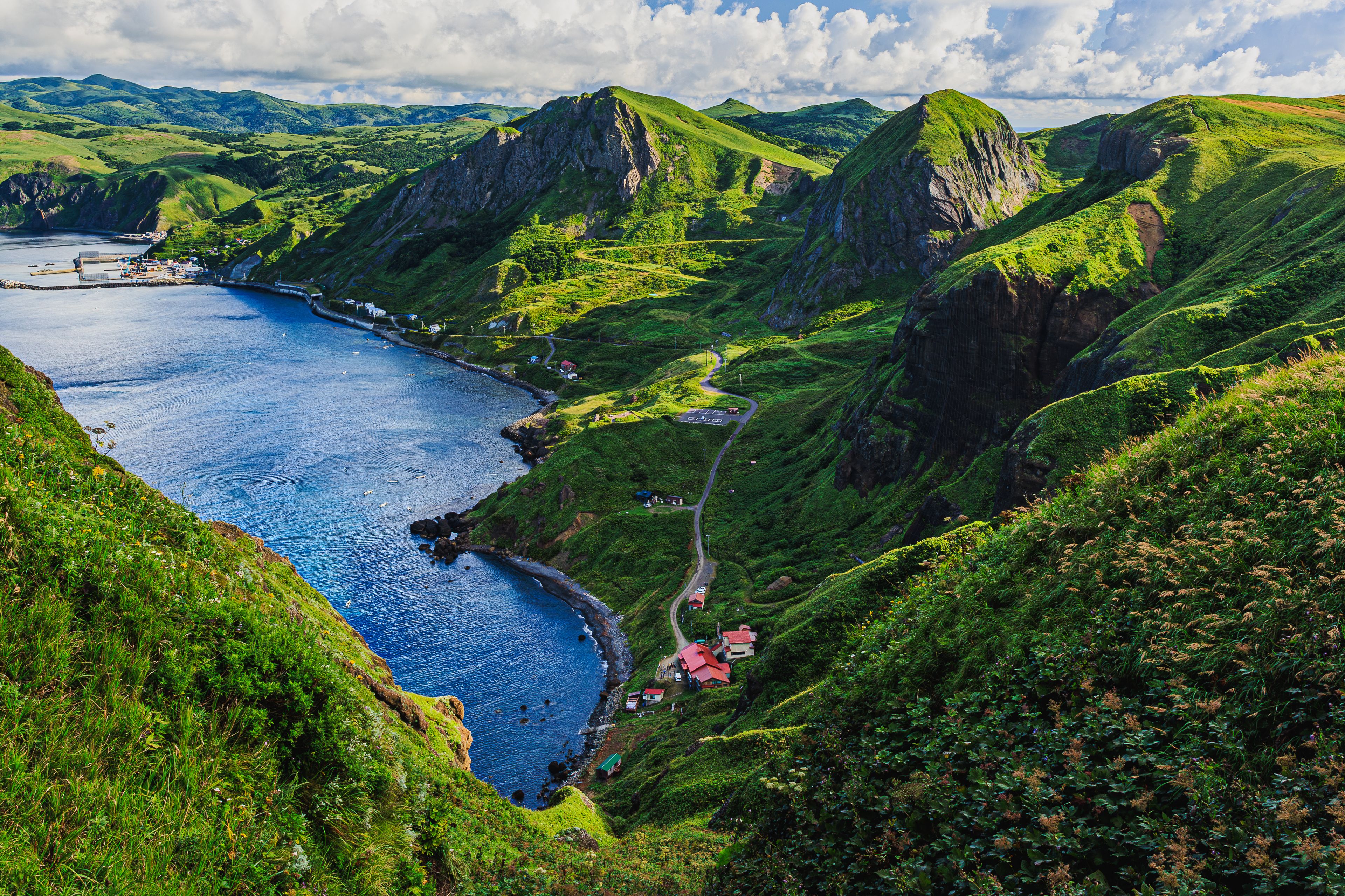 A coastal landscape with green hills, a winding road, and a body of water.