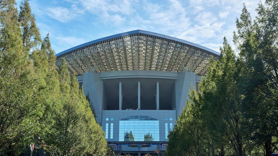 A modern building with a large glass facade and a distinctive roof structure.