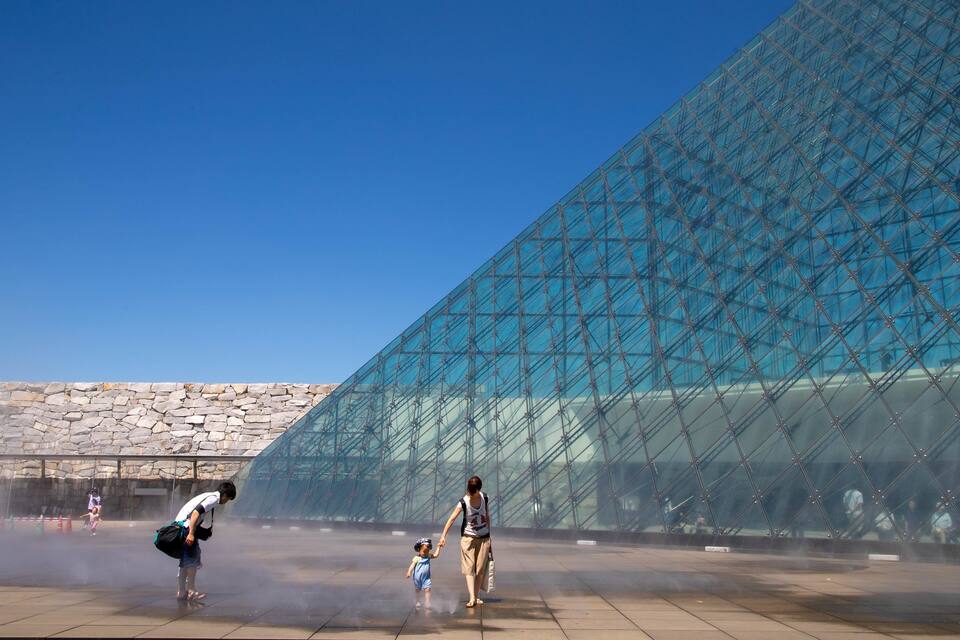 A large glass pyramid structure with a stone wall in the background.