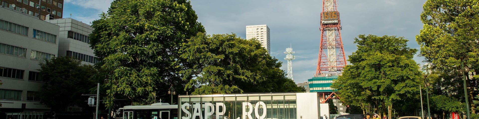 A park with a large sign reading "SAPPORO" and a tall tower in the background.