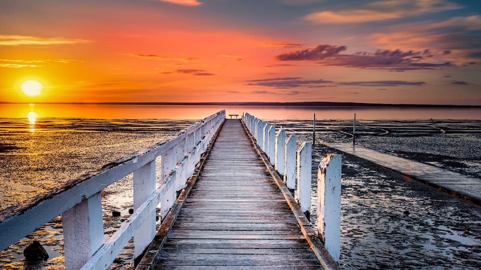 A wooden pier extending into a calm body of water during sunset.