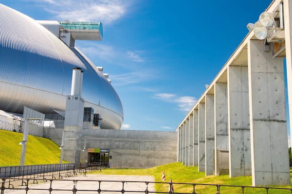 Um edifício grande e moderno com fachada metálica curva e um corredor de vidro.
