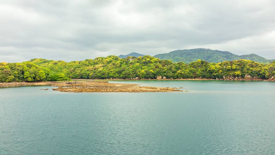 A calm lake surrounded by lush green hills and a cloudy sky.