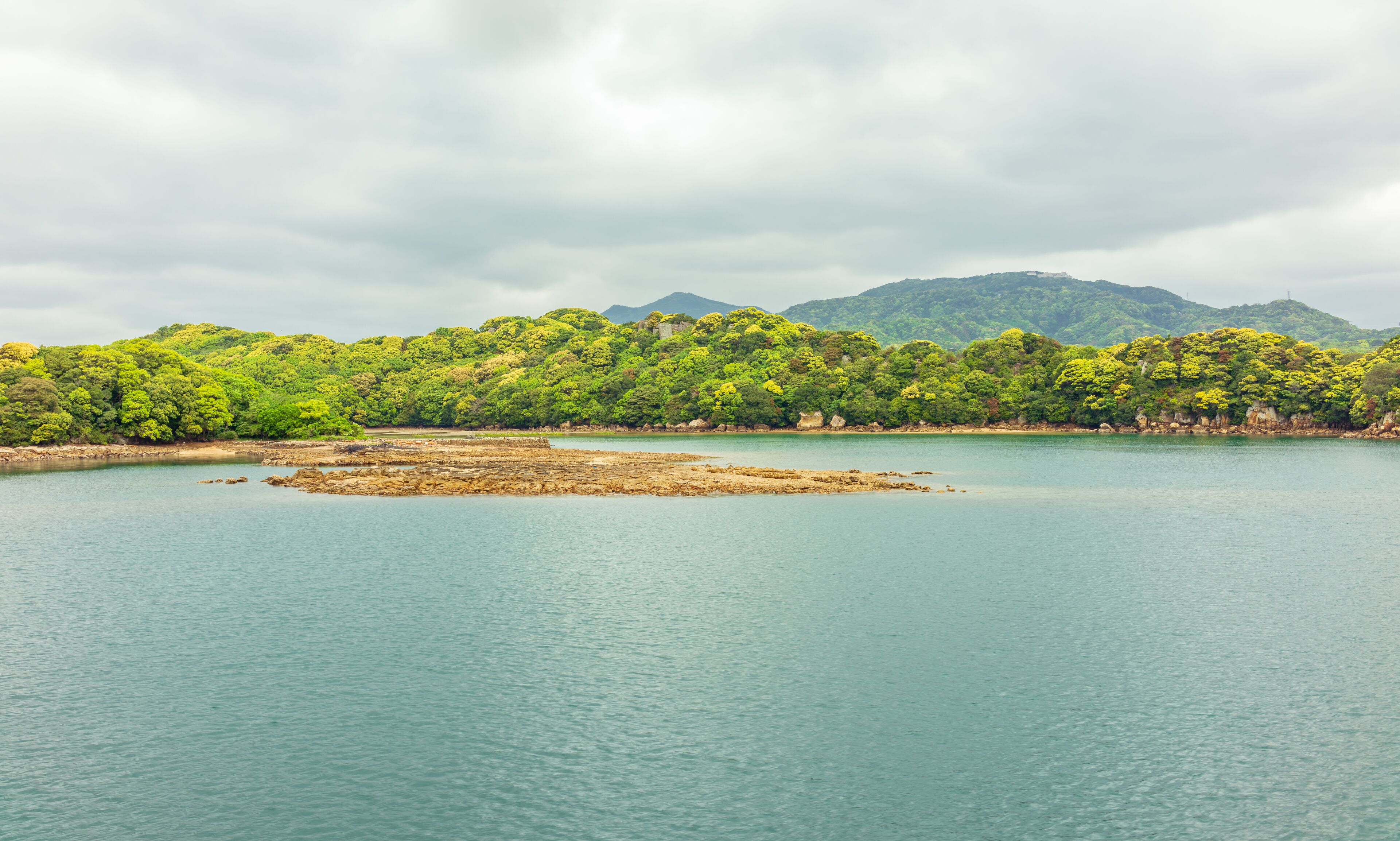 A calm lake surrounded by lush green hills and a cloudy sky.
